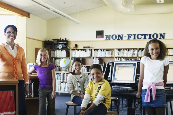 A librarian and 4 students are inside a library.